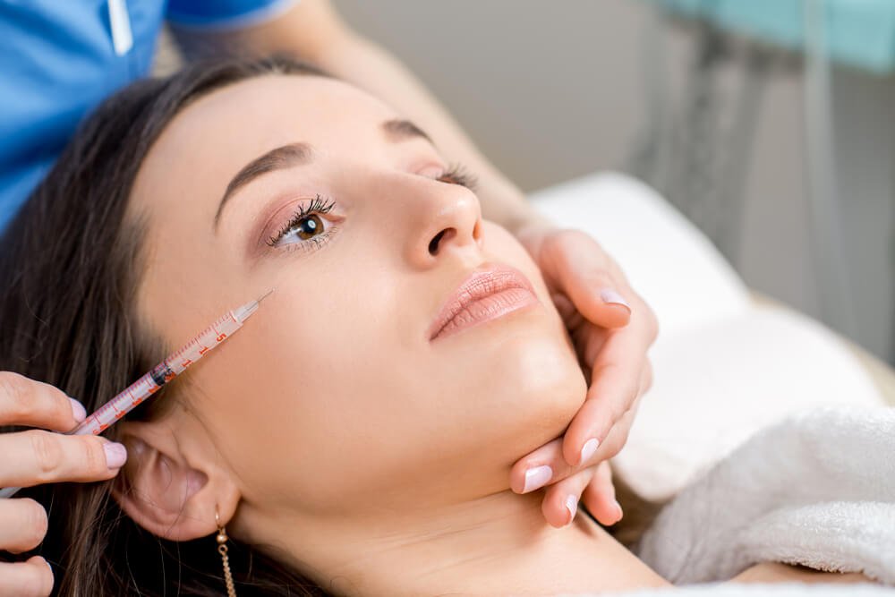 Woman Receiving a Botox Injection in the Eye Zone Lying in Bathrobe on the Medical Couch