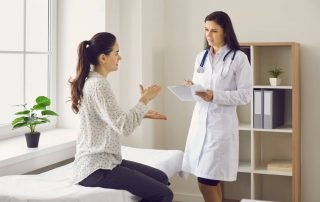 Woman Talking To Female Doctor Sitting on Examination Bed at Clinic