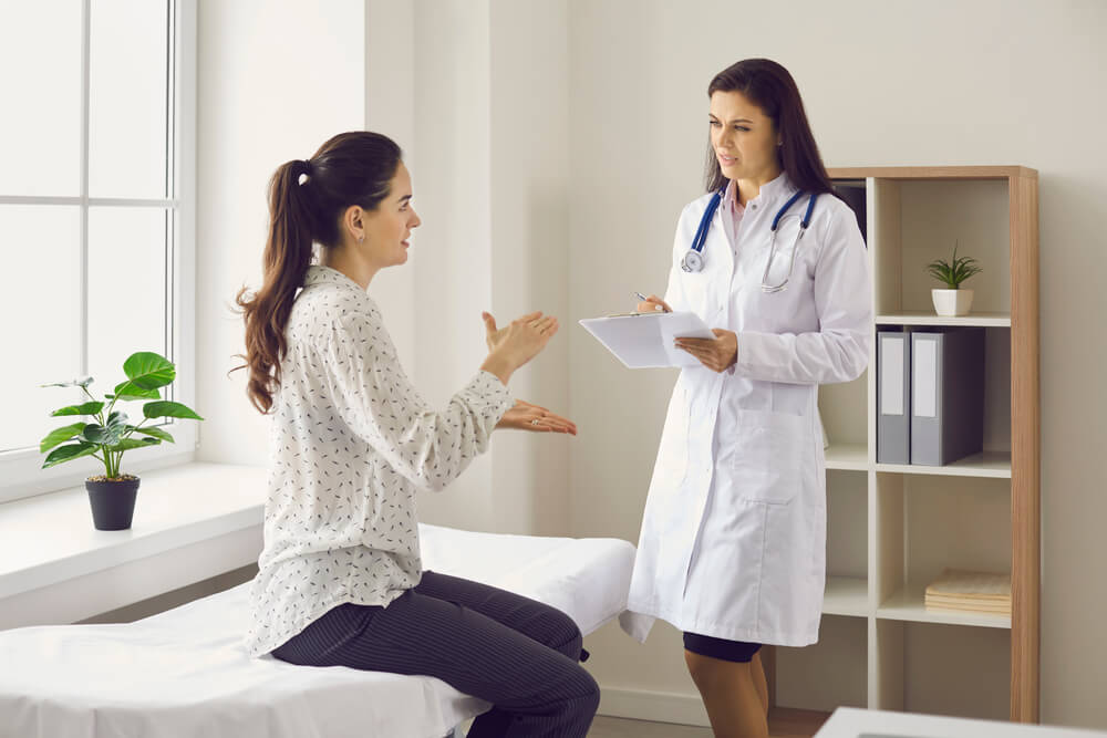 Woman Talking To Female Doctor Sitting on Examination Bed at Clinic